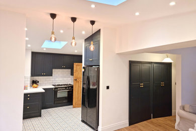 Medium sized contemporary cream and black l-shaped open plan kitchen in Manchester with a belfast sink, shaker cabinets, black cabinets, composite countertops, white splashback, metro tiled splashback, black appliances, porcelain flooring, no island, multi-coloured floors, white worktops, a vaulted ceiling and feature lighting.