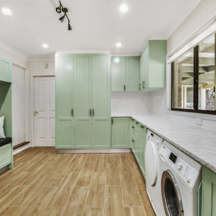 シドニーのトランジショナルスタイルのおしゃれな家事室 (シェーカースタイル扉のキャビネット、緑のキャビネット、ラミネートカウンター、グレーの壁、磁器タイルの床、左右配置の洗濯機・乾燥機、茶色い床、ドロップインシンク) の写真