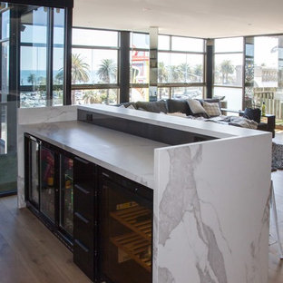 This is an example of a large modern galley breakfast bar in Melbourne with flat-panel cabinets, a built-in sink, black cabinets, tile countertops, grey splashback, mosaic tiled splashback, medium hardwood flooring, brown floors and white worktops.