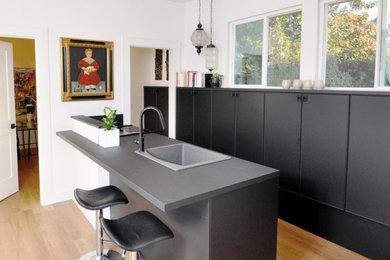 Inspiration for a small modern galley vinyl floor and beige floor open concept kitchen remodel in San Diego with a drop-in sink, flat-panel cabinets, black cabinets, laminate countertops, black backsplash, black appliances, a peninsula and black countertops