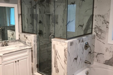 Inspiration for a mid-sized transitional master brown tile, white tile and marble tile porcelain tile and brown floor bathroom remodel in New York with raised-panel cabinets, white cabinets, gray walls, an undermount sink, quartz countertops, a hinged shower door and white countertops