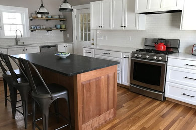 Photo of a transitional l-shaped eat-in kitchen in Boston with a double-bowl sink, white cabinets, white splashback, stainless steel appliances, with island, brown floor, subway tile splashback, medium hardwood floors and recessed-panel cabinets.