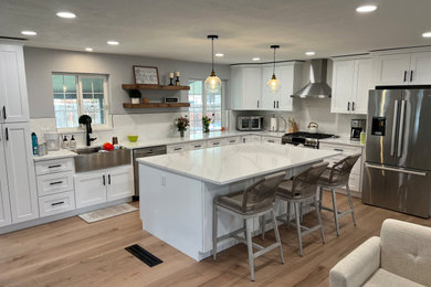 Example of a large minimalist l-shaped laminate floor and brown floor eat-in kitchen design in Denver with a farmhouse sink, shaker cabinets, white cabinets, marble countertops, white backsplash, ceramic backsplash, stainless steel appliances, an island and white countertops