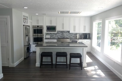 Kitchen pantry - modern single-wall black floor and bamboo floor kitchen pantry idea in Houston with recessed-panel cabinets, white cabinets, solid surface countertops, mosaic tile backsplash, stainless steel appliances, an island, black countertops and a double-bowl sink