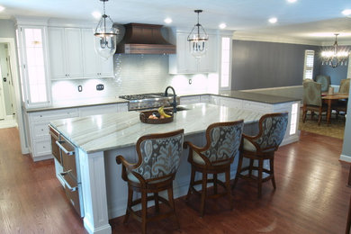 Open concept kitchen - mid-sized traditional l-shaped medium tone wood floor open concept kitchen idea in Other with white cabinets, quartzite countertops, glass tile backsplash, stainless steel appliances, an island, recessed-panel cabinets, white backsplash and a farmhouse sink