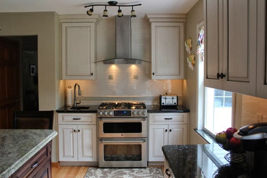 Eat-in kitchen - mid-sized traditional l-shaped light wood floor eat-in kitchen idea in Other with raised-panel cabinets, white cabinets, granite countertops, white backsplash, subway tile backsplash, stainless steel appliances and an island