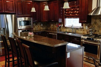 This is an example of a mid-sized traditional l-shaped eat-in kitchen in Orlando with an undermount sink, raised-panel cabinets, dark wood cabinets, granite benchtops, beige splashback, ceramic splashback, stainless steel appliances, light hardwood floors, with island and beige floor.