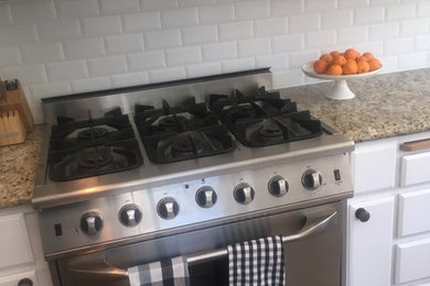 Eat-in kitchen - large traditional u-shaped dark wood floor and brown floor eat-in kitchen idea in San Francisco with a farmhouse sink, white cabinets, granite countertops, white backsplash, ceramic backsplash, stainless steel appliances, no island and multicolored countertops
