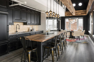 Inspiration for a large country single-wall eat-in kitchen in St Louis with a drop-in sink, raised-panel cabinets, black cabinets, wood benchtops, beige splashback, ceramic splashback, black appliances, painted wood floors, with island, grey floor and brown benchtop.