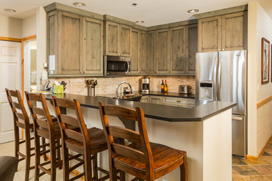 Eat-in kitchen - small transitional u-shaped slate floor eat-in kitchen idea in Denver with an undermount sink, shaker cabinets, distressed cabinets, granite countertops, beige backsplash, glass tile backsplash, stainless steel appliances and a peninsula