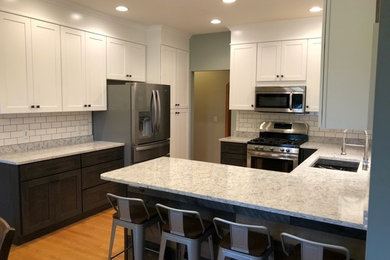 Example of a mid-sized transitional u-shaped light wood floor eat-in kitchen design in Other with shaker cabinets, quartz countertops, an undermount sink, white backsplash, subway tile backsplash, stainless steel appliances and gray countertops
