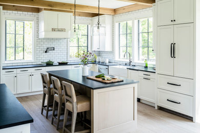Design ideas for a large country u-shaped separate kitchen in Bridgeport with a farmhouse sink, recessed-panel cabinets, white cabinets, quartz benchtops, white splashback, subway tile splashback, panelled appliances, light hardwood floors, with island, beige floor, black benchtop and exposed beam.