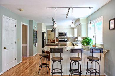 Inspiration for a mid-sized transitional l-shaped light wood floor enclosed kitchen remodel in Other with a single-bowl sink, shaker cabinets, white cabinets, granite countertops, beige backsplash, stone tile backsplash, stainless steel appliances and two islands