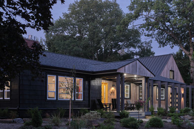 Photo of a mid-sized contemporary one-storey black house exterior in Other with wood siding, a gable roof, a metal roof, a black roof and board and batten siding.