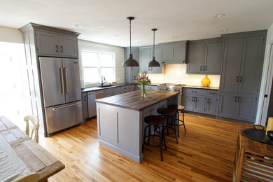Inspiration for a mid-sized l-shaped light wood floor eat-in kitchen remodel in New York with flat-panel cabinets, gray cabinets, soapstone countertops, white backsplash, stainless steel appliances and an island