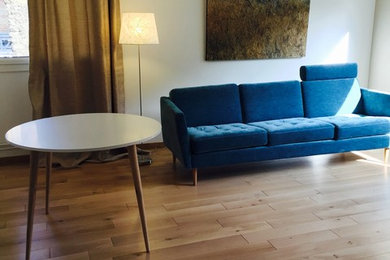 Cette image montre un grand salon design fermé avec un mur blanc, un sol en bois brun, un téléviseur dissimulé et un sol beige.