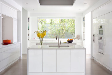 Large trendy u-shaped light wood floor eat-in kitchen photo in Denver with an undermount sink, glass-front cabinets, white cabinets, quartz countertops, white backsplash, white appliances and two islands
