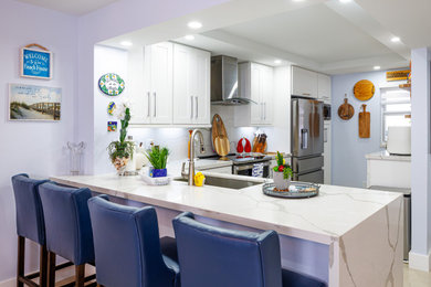 Example of a mid-sized trendy l-shaped porcelain tile, beige floor and vaulted ceiling eat-in kitchen design in Miami with a single-bowl sink, shaker cabinets, white cabinets, quartz countertops, white backsplash, quartz backsplash, stainless steel appliances, a peninsula and white countertops