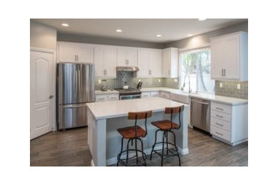 Example of a mid-sized minimalist l-shaped porcelain tile and gray floor open concept kitchen design in Philadelphia with a farmhouse sink, shaker cabinets, white cabinets, granite countertops, gray backsplash, subway tile backsplash, stainless steel appliances and an island