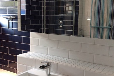 Medium sized modern family bathroom in London with a built-in bath, a shower/bath combination, a one-piece toilet, blue tiles, ceramic tiles, blue walls, ceramic flooring, a wall-mounted sink, white floors and a hinged door.