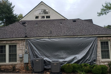Large 1960s yellow two-story stone house exterior idea in Other with a hip roof, a shingle roof and a black roof