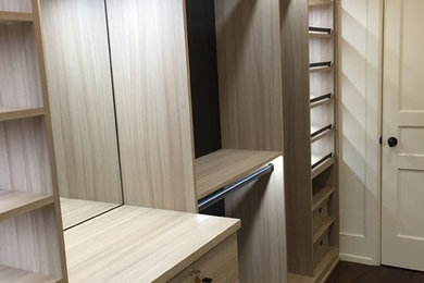 Inspiration for a mid-sized transitional gender-neutral dark wood floor and brown floor walk-in closet remodel in New York with flat-panel cabinets and light wood cabinets
