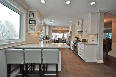 Large transitional galley porcelain tile and brown floor eat-in kitchen photo in Edmonton with an undermount sink, stainless steel appliances, raised-panel cabinets, white cabinets, granite countertops, beige backsplash, stone tile backsplash and a peninsula