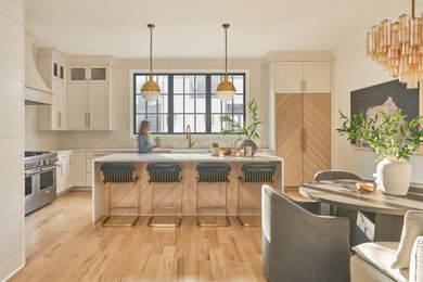 Example of a transitional l-shaped light wood floor eat-in kitchen design in Charlotte with shaker cabinets, white cabinets, white backsplash, stainless steel appliances, an island and white countertops