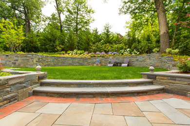 Photo of a traditional backyard garden for summer in New York with a retaining wall and natural stone pavers.