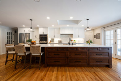 Example of a large classic medium tone wood floor kitchen design in Other with an undermount sink, recessed-panel cabinets, white cabinets, quartz countertops, white backsplash, subway tile backsplash, stainless steel appliances, an island and white countertops