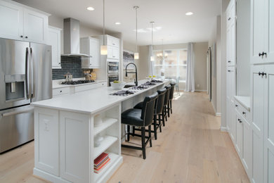 Inredning av ett modernt mellanstort vit vitt kök, med en undermonterad diskho, skåp i shakerstil, vita skåp, bänkskiva i kvartsit, grått stänkskydd, stänkskydd i glaskakel, rostfria vitvaror, ljust trägolv, en köksö och flerfärgat golv