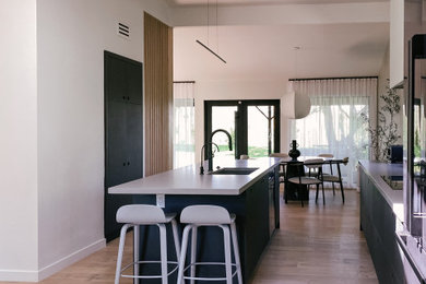 Photo of a mid-sized modern single-wall eat-in kitchen in Los Angeles with an undermount sink, flat-panel cabinets, blue cabinets, granite benchtops, white splashback, granite splashback, stainless steel appliances, light hardwood floors, with island, multi-coloured floor, white benchtop and vaulted.