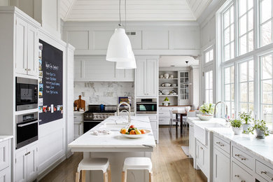 Elegant light wood floor and beige floor kitchen photo in New York with gray cabinets, marble countertops, marble backsplash, an island, a farmhouse sink, shaker cabinets, white backsplash and stainless steel appliances