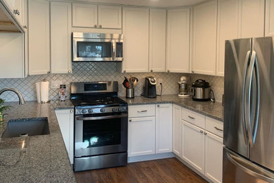 Mid-sized transitional u-shaped eat-in kitchen in Cleveland with an undermount sink, shaker cabinets, white cabinets, granite benchtops, white splashback, mosaic tile splashback, stainless steel appliances, medium hardwood floors, a peninsula, brown floor and grey benchtop.