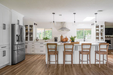 Inspiration for a large modern u-shaped medium tone wood floor and brown floor eat-in kitchen remodel in Orlando with a single-bowl sink, glass-front cabinets, white cabinets, quartzite countertops, white backsplash, ceramic backsplash, stainless steel appliances, an island and white countertops