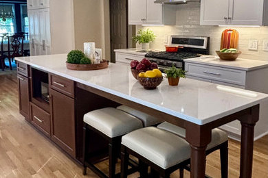 Inspiration for a mid-sized transitional light wood floor and brown floor open concept kitchen remodel in Cleveland with a single-bowl sink, flat-panel cabinets, white cabinets, quartz countertops, white backsplash, subway tile backsplash, stainless steel appliances, an island and white countertops