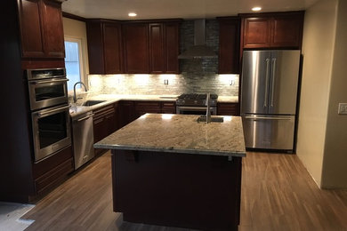 Small elegant l-shaped medium tone wood floor and brown floor eat-in kitchen photo in San Francisco with a single-bowl sink, raised-panel cabinets, medium tone wood cabinets, granite countertops, white backsplash, glass tile backsplash, stainless steel appliances and an island