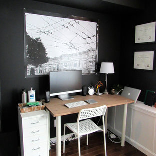 Bild på ett litet eklektiskt hemmabibliotek, med svarta väggar, mörkt trägolv och ett fristående skrivbord