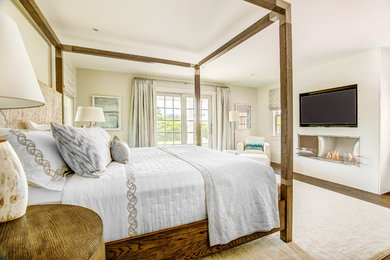 Large beach style master medium tone wood floor and brown floor bedroom photo in Other with white walls, a ribbon fireplace and a wood fireplace surround