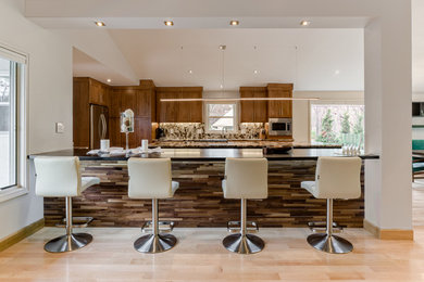 This is an example of a large contemporary galley eat-in kitchen in Columbus with an undermount sink, recessed-panel cabinets, medium wood cabinets, granite benchtops, multi-coloured splashback, stone slab splashback, stainless steel appliances, light hardwood floors and with island.