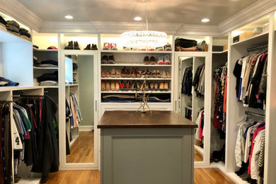 Large transitional gender-neutral walk-in wardrobe in New York with open cabinets, yellow cabinets, medium hardwood floors and brown floor.