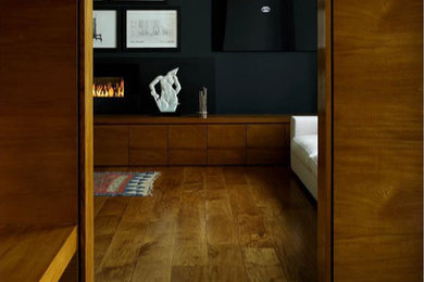 This is an example of a medium sized contemporary enclosed living room in London with a reading nook, black walls, medium hardwood flooring, a standard fireplace, a built-in media unit and brown floors.