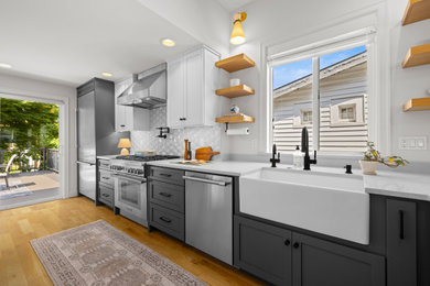 Inspiration for a craftsman l-shaped light wood floor and brown floor open concept kitchen remodel in Seattle with a farmhouse sink, shaker cabinets, gray cabinets, quartz countertops, white backsplash, ceramic backsplash, stainless steel appliances, two islands and white countertops