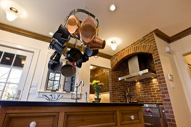 Example of a mid-sized classic u-shaped medium tone wood floor enclosed kitchen design in Chicago with a farmhouse sink, beaded inset cabinets, distressed cabinets, granite countertops, beige backsplash, stone tile backsplash and paneled appliances