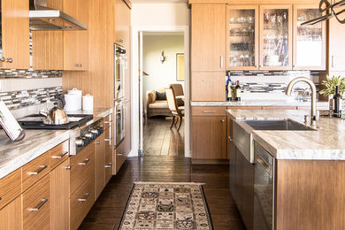 Inspiration for a large transitional l-shaped medium tone wood floor and brown floor open concept kitchen remodel in Other with a farmhouse sink, flat-panel cabinets, light wood cabinets, granite countertops, glass tile backsplash, stainless steel appliances and an island