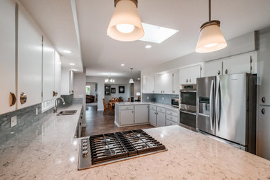 Mid-sized minimalist l-shaped vinyl floor, brown floor and coffered ceiling eat-in kitchen photo in Portland with a drop-in sink, flat-panel cabinets, white cabinets, quartzite countertops, blue backsplash, glass tile backsplash, stainless steel appliances, a peninsula and gray countertops