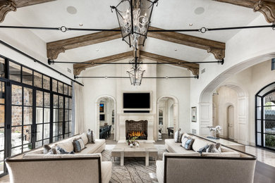 French country open concept medium tone wood floor, brown floor and exposed beam family room photo in Phoenix with beige walls, a standard fireplace, a stone fireplace and a media wall