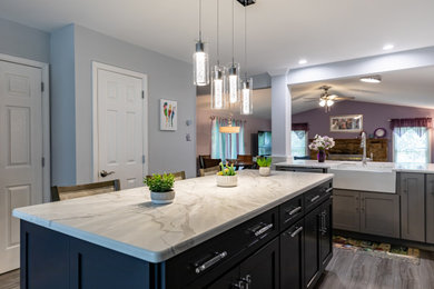 Example of a mid-sized classic l-shaped medium tone wood floor and gray floor open concept kitchen design in Philadelphia with a farmhouse sink, shaker cabinets, quartz countertops, blue backsplash, porcelain backsplash, stainless steel appliances, an island and beige countertops