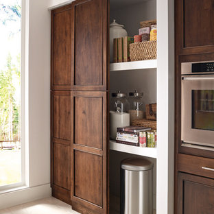 Aménagement d'une grande arrière-cuisine linéaire classique avec un îlot central, un évier encastré, un placard avec porte à panneau encastré, des portes de placard en bois brun, un électroménager en acier inoxydable, un sol en bois clair et un sol beige.