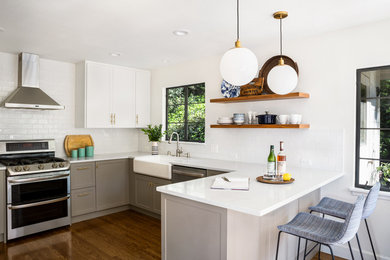 Transitional u-shaped dark wood floor and brown floor kitchen photo in Denver with a farmhouse sink, shaker cabinets, white cabinets, white backsplash, subway tile backsplash, stainless steel appliances, a peninsula and white countertops